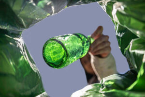 Person placing a green glass bottle into a collection bag for glass recycling.